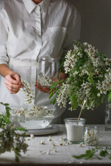 Woman wearing in white dress put acacia flowers in a plate with water. Girl prepares acacia jam.