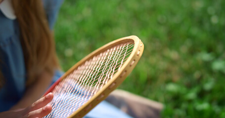 Closeup girl hand touching racket strings. Kid sitting on lush green lawn