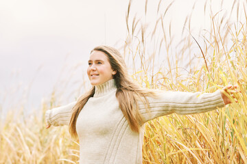 Fall portrait of young pretty girl posing outside with pampas grass, wearing warm beige pullover, windy day