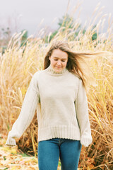 Fall portrait of young pretty girl posing outside with pampas grass, wearing warm beige pullover,...