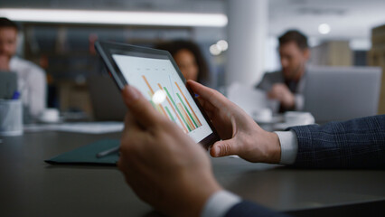 Serious businessman searching tablet looking graph charts on corporate meeting.