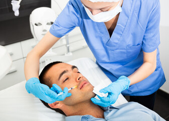 Woman doctor giving rejuvenating injections with syringe for facial correction to male patient in beauty clinic