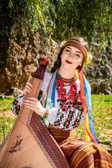 Ukrainian musician in authentic national dress sits by a rock