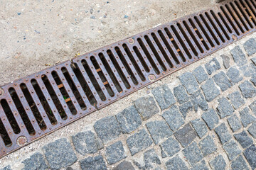 Grating of drainage system rainwater in the park at the sidewalk from a stone shaped paving slabs