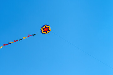 A colorful round kite soars high in the sky Blue sky. Sports kite festival. Clean Monday in Greece. A flying kite with a wriggling tail. Copyspace.
