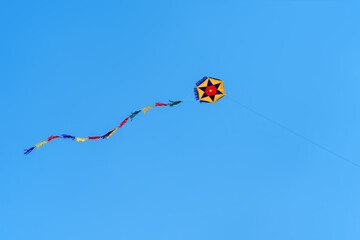 A colorful round kite soars high in the sky Blue sky. Sports kite festival. Clean Monday in Greece. A flying kite with a wriggling tail. Copyspace.
