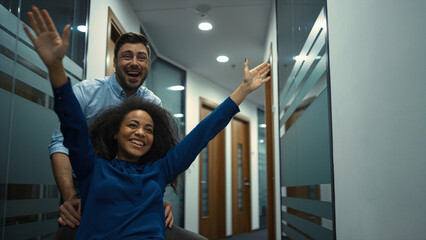 Multiethnic business team celebrating success in company. Office chair race.