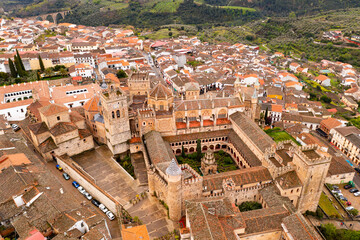 Gothic-Mudejar style building of Royal Monastery of Saint Mary in Spanish town of Guadalupe, located in green valley of province of Caceres overlooking brownish roofs of houses, as seen from drone..