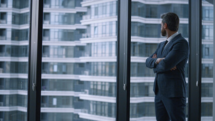 Successful businessman crossing hands looking window wall in corporate building.