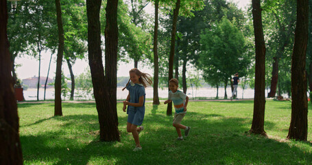 Laughing children running on sunny meadow. Happy kids play catch-up in park.