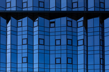 Mirrored facade of building with small square windows. Glazing of facade with blue glass. Architectural background
