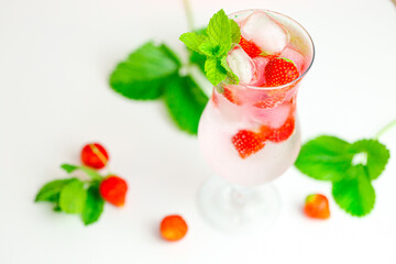 Strawberry drink.Refreshing summer cocktail.Summer drink.mineral water glass with ice and ripe strawberries with leaves on a pink background.Drink from summer berries