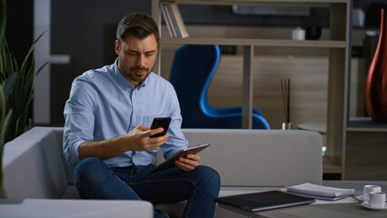 Corporate man calling phone looking tablet research business data in home office