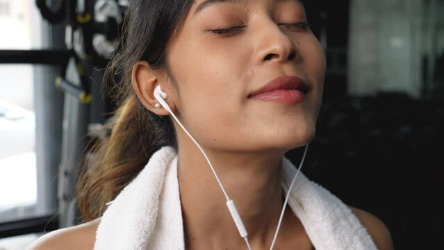 Close up image, happy smiling asian woman in earphones listening music while being in gym