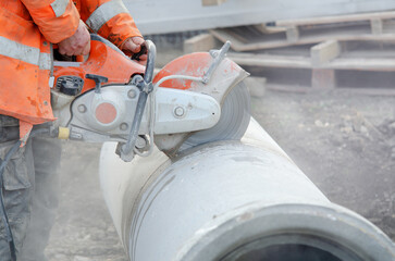 A worker at the construction site cutting a concrete drainage pipe with a concrete saw..Builder...