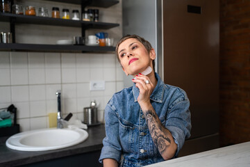 One woman mature caucasian female using gua sha rose quartz face massage stone in the kitchen at...