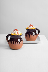 two corn in a cup, Esquite, Mexican snack in clay glasses with white cheese and chili powder on a white table and a minimalist white background, ready to eat