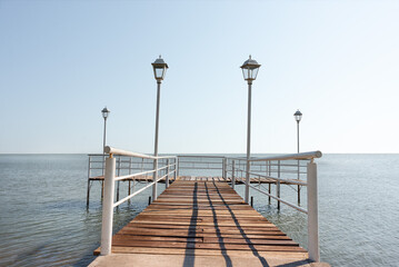 Wooden and metal pier with lampposts during a cloudless summer day with a calm sea without boats