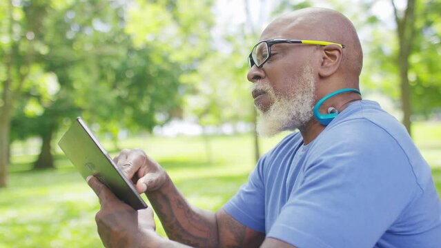 Senior black man scrolling on his digital tablet device outdoors, in slow motion