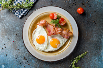 Fried eggs with tomatoes and bacon on blue concrete table top view