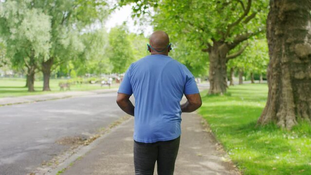 Camera following a senior black man jogging in a park one day, in slow motion