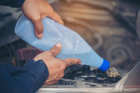Car Mechanic man hands pouring Deionized purified Distilled water for car battery mechanical service. Close up hands man hold Deionized Distilled liquid water bottle at garage auto mobile car service