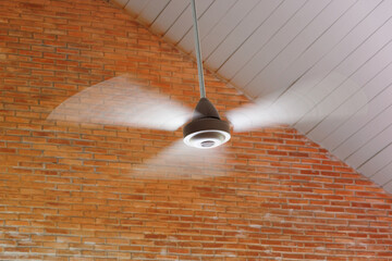 Moving white ceiling fan on white ceiling and brick wall background.