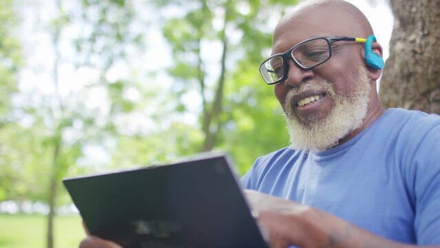 Senior Black Male Using A Digital Tablet, Smiles As He Reads Something On His Device, In Slow Motion