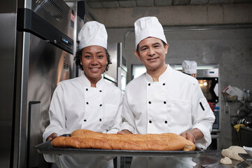 Portrait of professional chefs in white uniform looking at camera with cheerful smile and proud with tray of baguette in kitchen. Friend and partner of pastry foods and fresh daily bakery occupation.