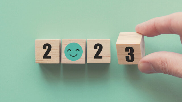 Hands holding 2023 with smile face wooden blocks, Happy New Year, positive mental health plan, optimistic resolution goal, eco sustainable target concept