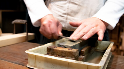 Master swordsmith is sharpening knife on grindstone with water