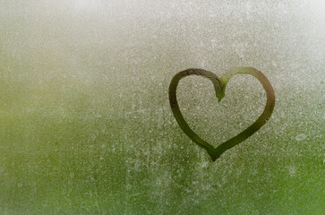 Heart painted on window which fogged up after rain with blurred green color background.