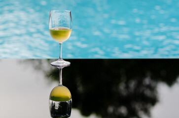 A glass of white wine puts on table at swimming pool for Holiday and summer drink concept.