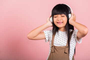 Asian little kid 10 years old smiling listening music wearing wireless headset at studio shot isolated on pink background, Happy child girl lifestyle listen music with headphones keeping eyes closed