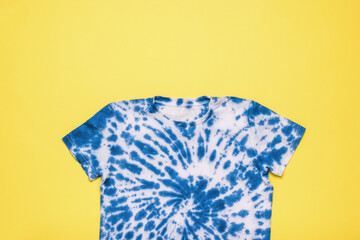 Blue tie dye T-shirt on a yellow background. Flat lay. - obrazy, fototapety, plakaty
