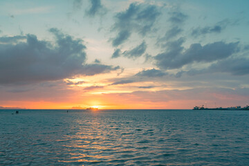The sun setting in the sea against the backdrop of the islands and the sailing ferry.  Colored skies over the sea.  People stand on a sandy spit in the sea and enjoy the sunset.