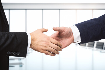 Two businessmen shake hands on the background of bright conference room, investing concept, close up