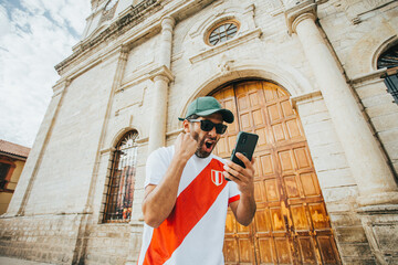 Hincha peruano de futbol celebrando un gol mirando su telefono en un parque de peru. Concepto de Personas y deportes. - obrazy, fototapety, plakaty