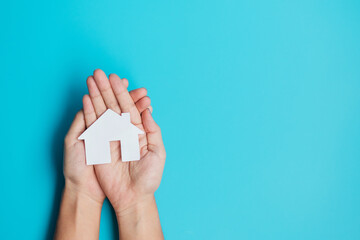 hand holding paper Home cutout on blue background. Real estate, Mortgage, Insurance, Rental, Happy...