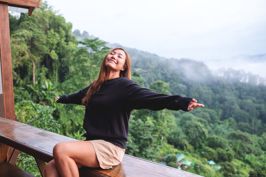 Portrait image of a young woman opening arms and enjoy a beautiful foggy mountain and nature view