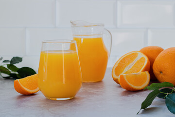Orange juice in a glass and in a jug and fresh oranges, green leaves. Photo on a light background.