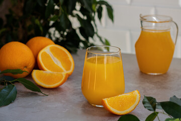 A glass of orange juice, fresh oranges and green foliage in the background. A corner in the kitchen.