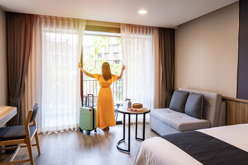 Young woman traveler opening the curtains and looking at the view from the window of a hotel room while on summer vacation, Travel lifestyle concept - obrazy, fototapety, plakaty