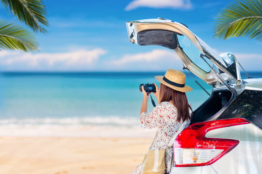 Young woman traveler taking a photo at the beautiful tropical beach with her car while travel driving road trip on summer vacation