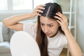 Damaged Hair, face serious asian young woman worry looking at scalp in mirror, hand in break into front hair loss, thin problem symptom at home. Health care shampoo beauty, isolated on background.