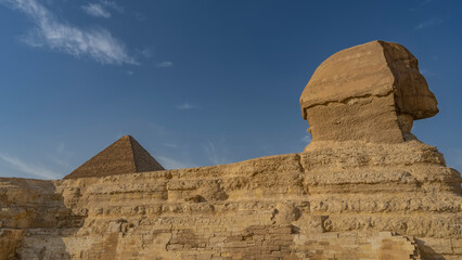 Sculpture of the Great Sphinx against the blue sky. Close-up. Profile view. The layered structure of the statue, the masonry is visible. The top of the pyramid above the back. Egypt. Giza