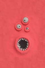 Monster with three ugly eyes and a mouth with sharp teeth, fabulous creature made by hand from pink plasticine. Comic facial expressions. Ugly and crazy face of alien monster. 3d artwork