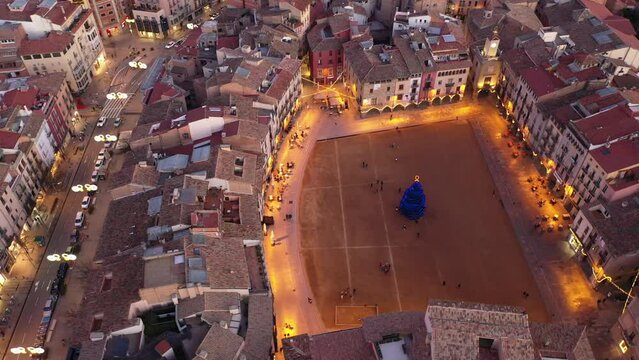 Aerial view of Spanish town of Vic overlooking central square decorated with festive lighting and main Christmas tree on eve of holidays in winter evening. High quality 4k footage