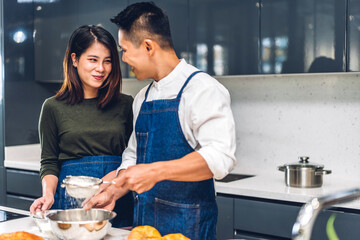Young asian family couple having fun cooking together with dough for homemade bake cookie and cake ingredient on table.Happy couple looking to preparing food the dough in kitchen