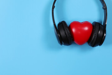 Fototapeta na wymiar Black headphones with red hearts isolated on light blue background. Flat lay photography has copy space.